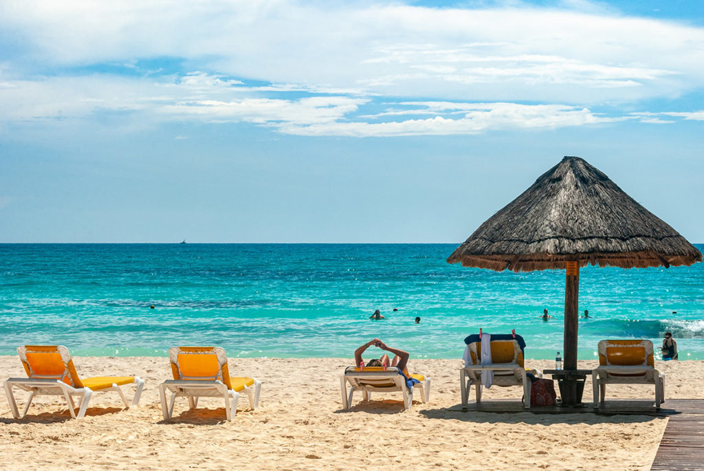 Multiple orange beach loungers with a tiki umbrella overlooking the ocean
